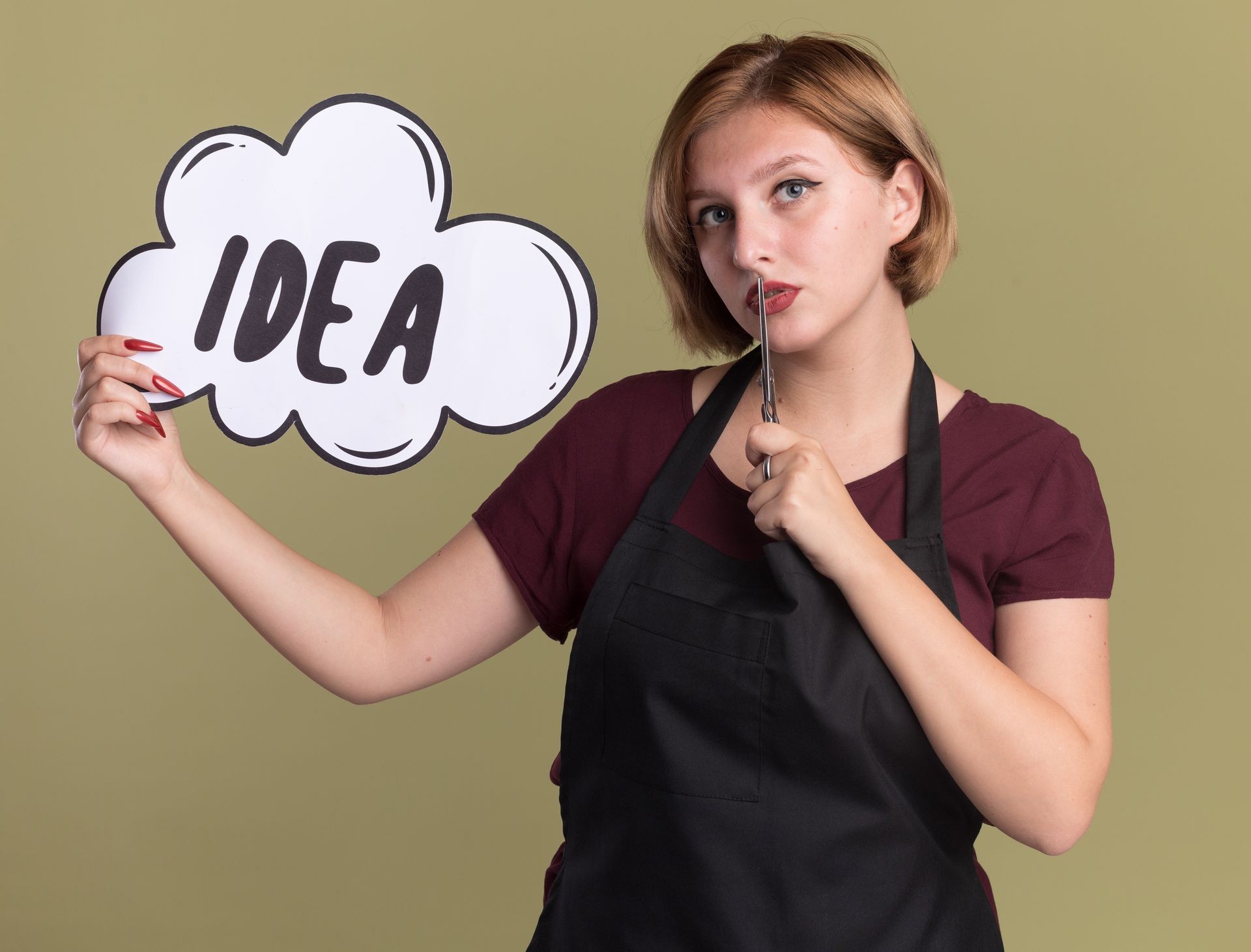 Person in apron holding an 'IDEA' sign and a pen, looking thoughtful.