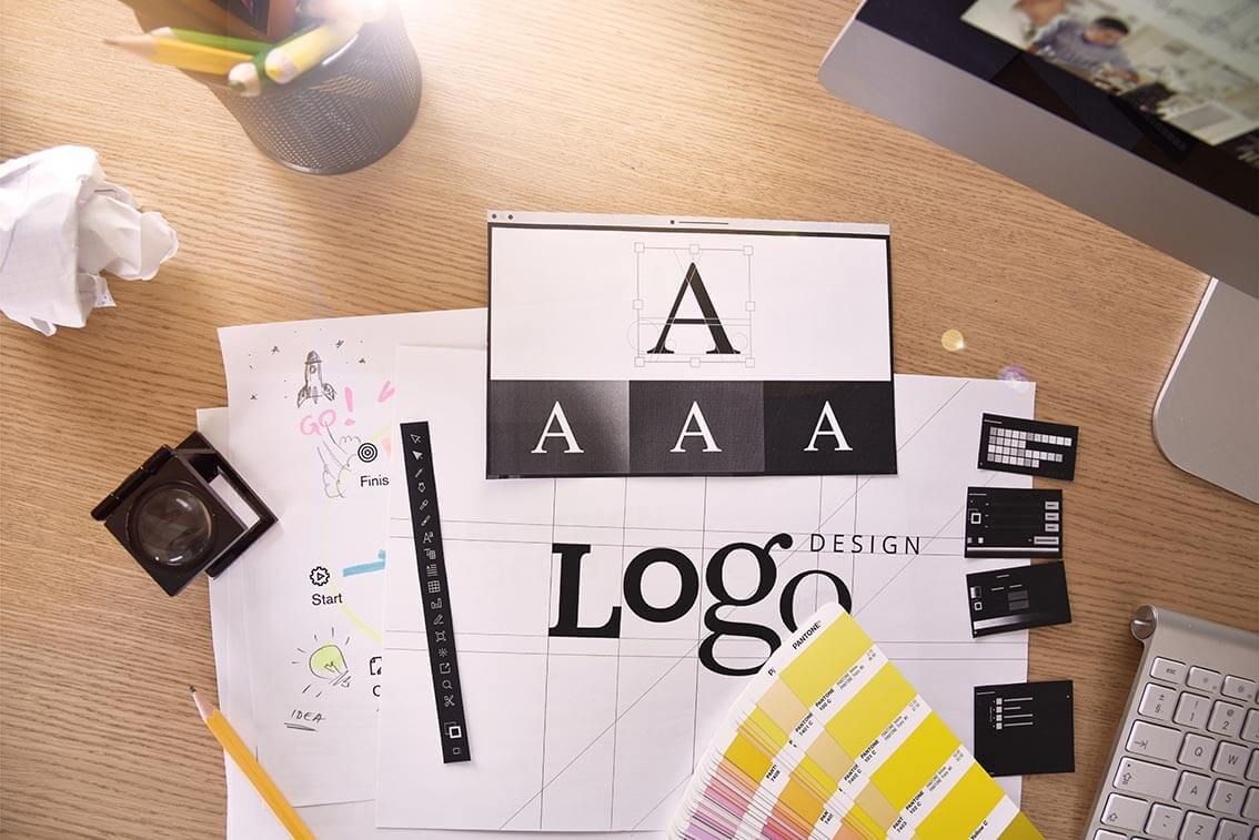 Desk with logo design drafts, color swatches, pencil holder, and computer keyboard.