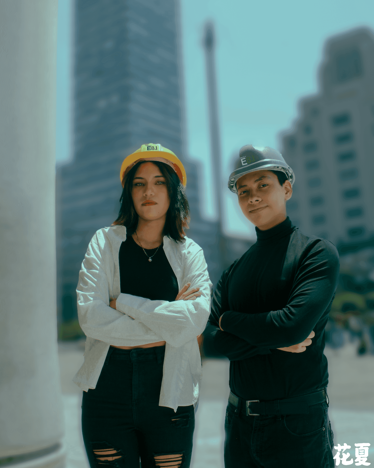 Two people in hard hats standing confidently in an urban setting with a skyscraper in the background.