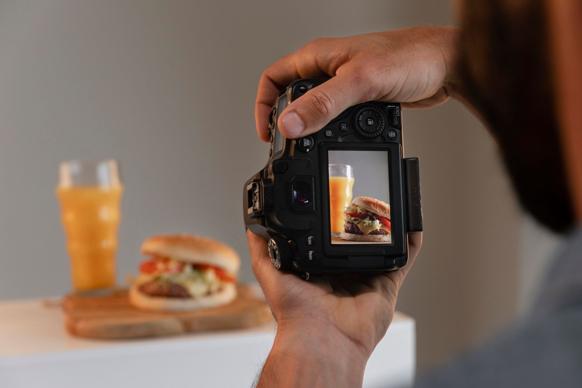 Person photographing a hamburger and a glass of orange juice with a camera in close view.